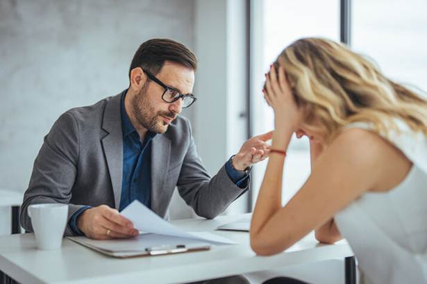 Man talking to stressed woman in office - Hostile Work Environment